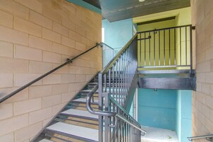 Una escalera con barandales de metal y pasamanos, que lleva a una puerta con reja.