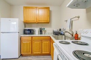Una cocina compacta con armarios de madera, refrigerador, microondas, estufa y pileta.