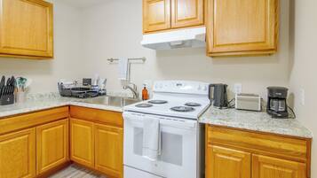A kitchen with wooden cabinets, a stove, a sink, and a coffee maker.