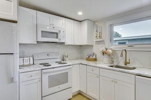 A kitchen with white cabinetry, a built-in microwave, a stove, a sink, and a window with a view. - Sun, Surf & Seafood: York Home 2 Blocks to Beach (York Beach)