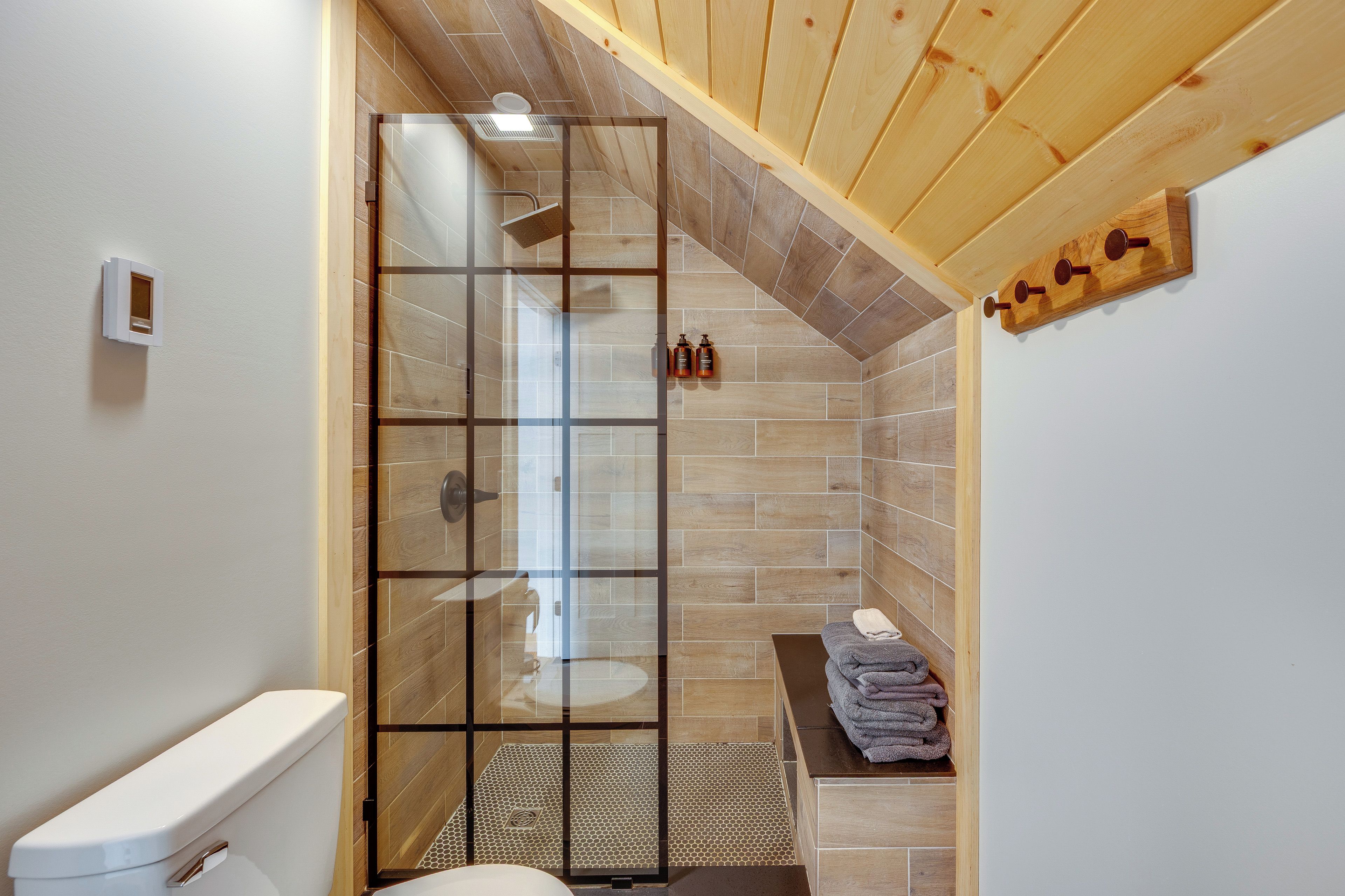 A bathroom with a glass shower enclosure, wooden flooring, and a towel rack.