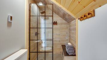 A bathroom with a glass shower enclosure, wooden flooring, and a towel rack.
