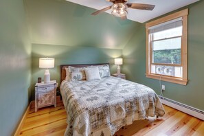 Un dormitorio con cama, dos lámparas de noche, ventilador de techo, ventana y suelo de madera.