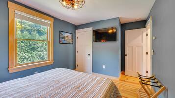 Un dormitorio con cama, ventana con persianas, un cuadro, televisor y puerta.