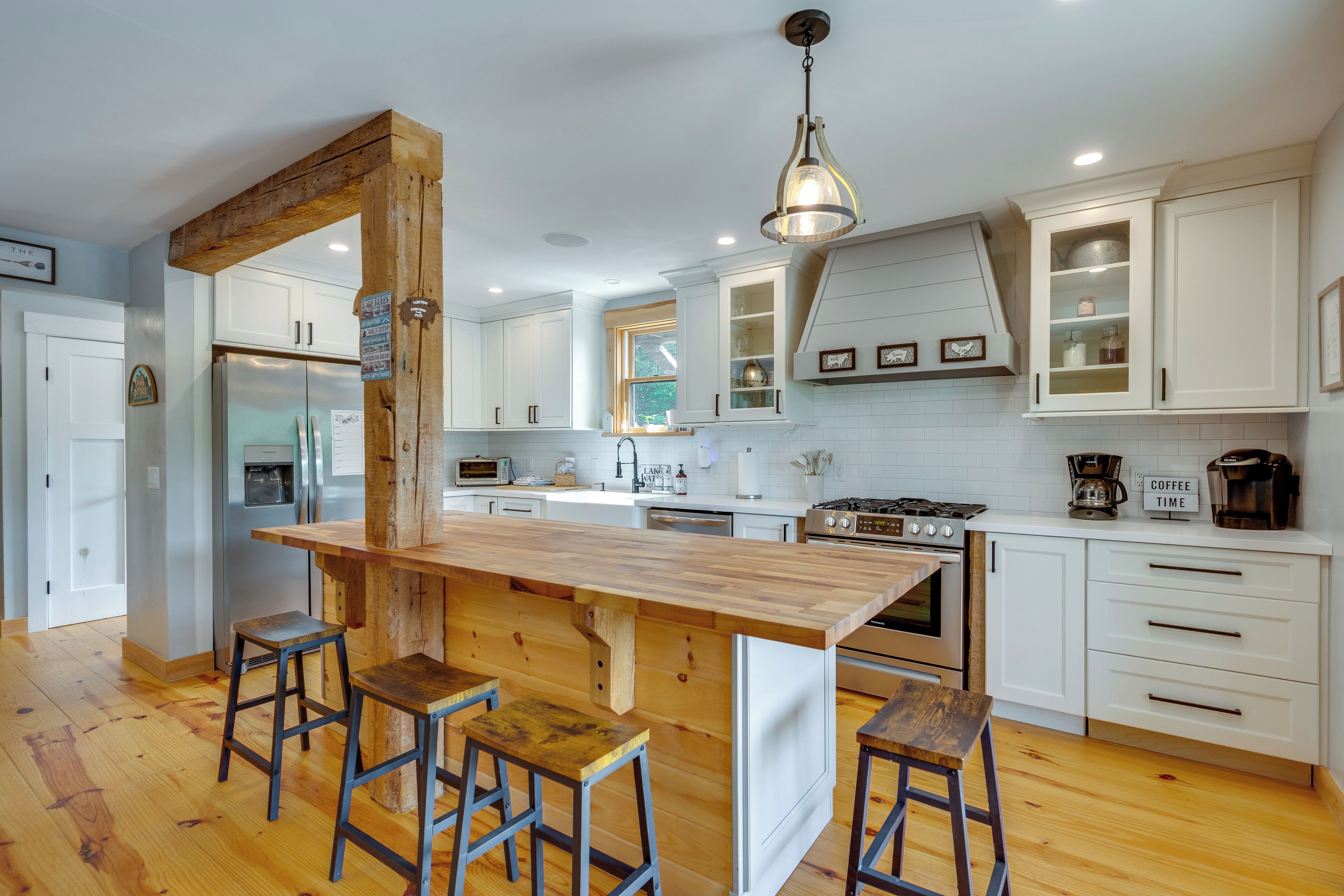 A modern kitchen with a central island, bar stools, white cabinetry, and stainless steel appliances.