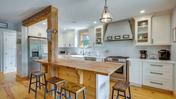 A modern kitchen with a central island, bar stools, white cabinetry, and stainless steel appliances.