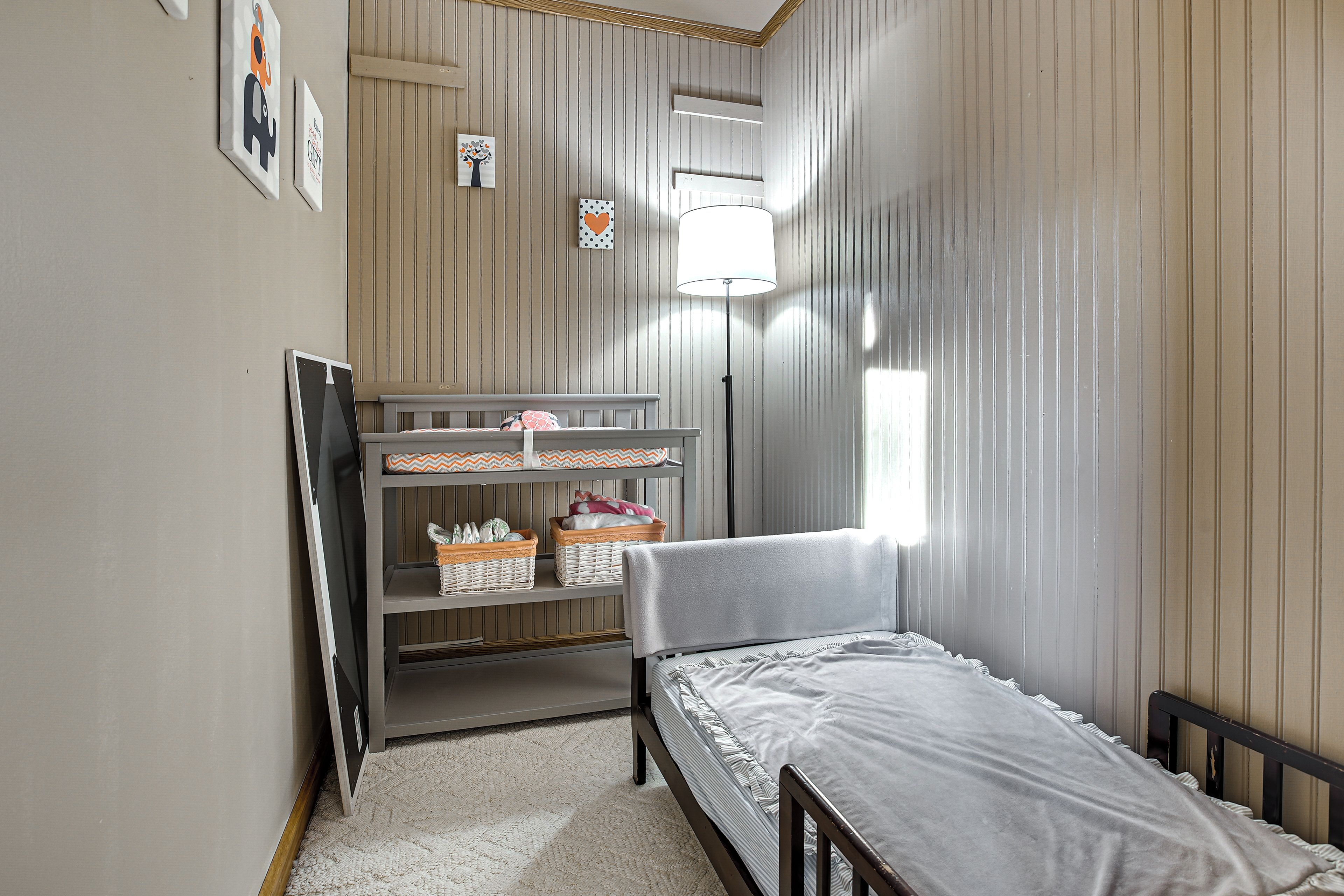 Une chambre à coucher comprenant un lit, une table de chevet, une lampe, une étagère avec des paniers et un téléviseur fixé au mur.