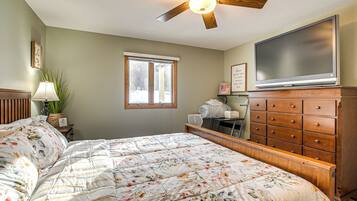 A bedroom with a bed, dresser, television, window, and ceiling fan.