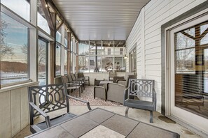 A covered outdoor seating area with chairs and tables, large windows, and a view of the surrounding landscape.