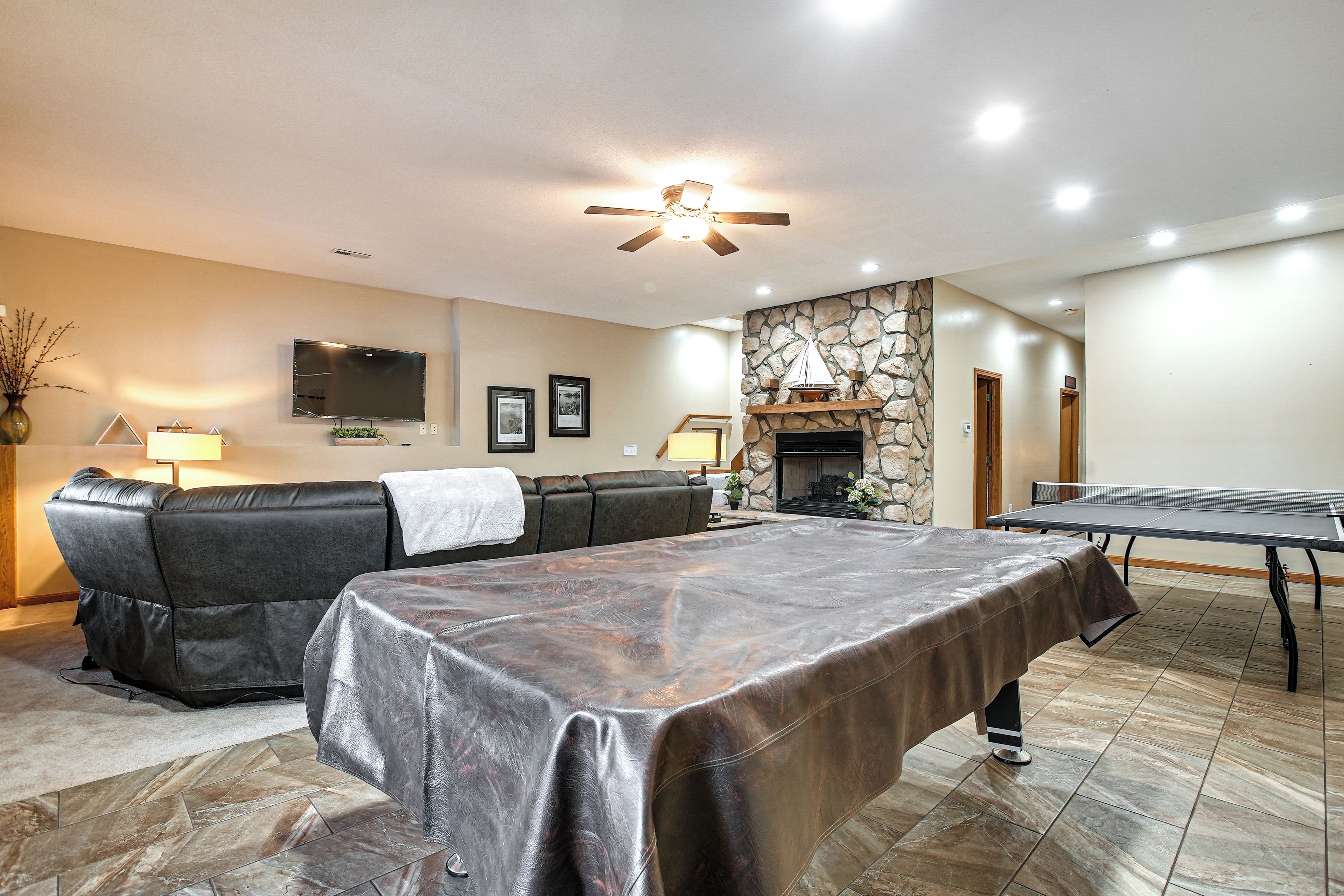 A living room with a leather sofa, a ping pong table, a stone fireplace, and a ceiling fan.