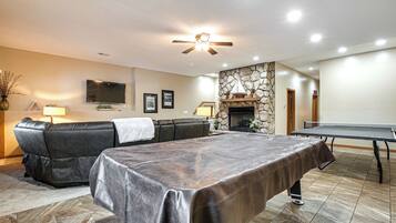 A living room with a leather sofa, a ping pong table, a stone fireplace, and a ceiling fan.
