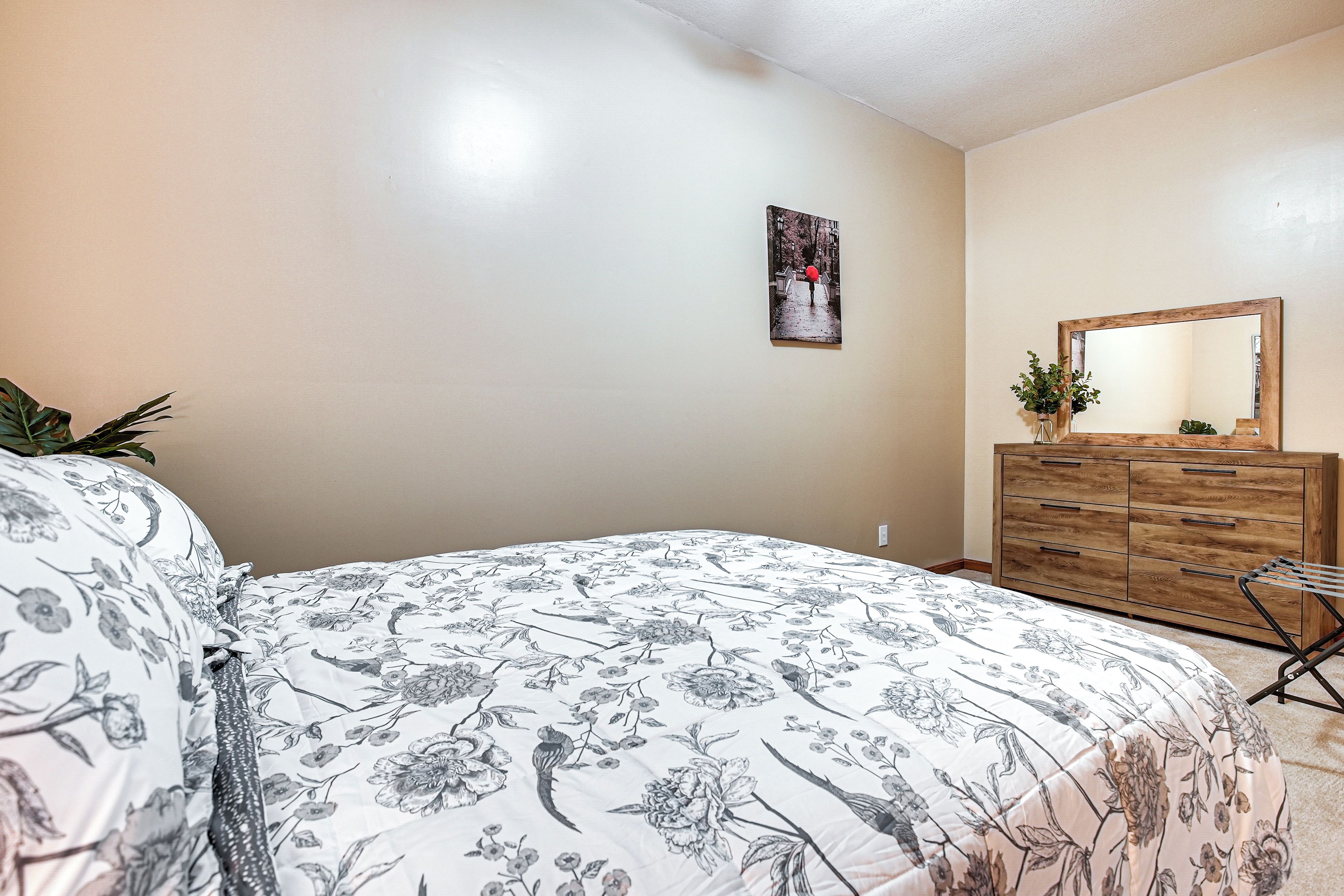 Un dormitorio con cama, cómoda, espejo y un cuadro en la pared.
