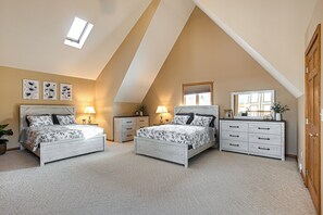 A bedroom with two beds, a dresser, and a skylight.