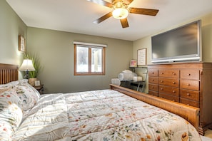 A bedroom with a bed, dresser, television, window, and ceiling fan.