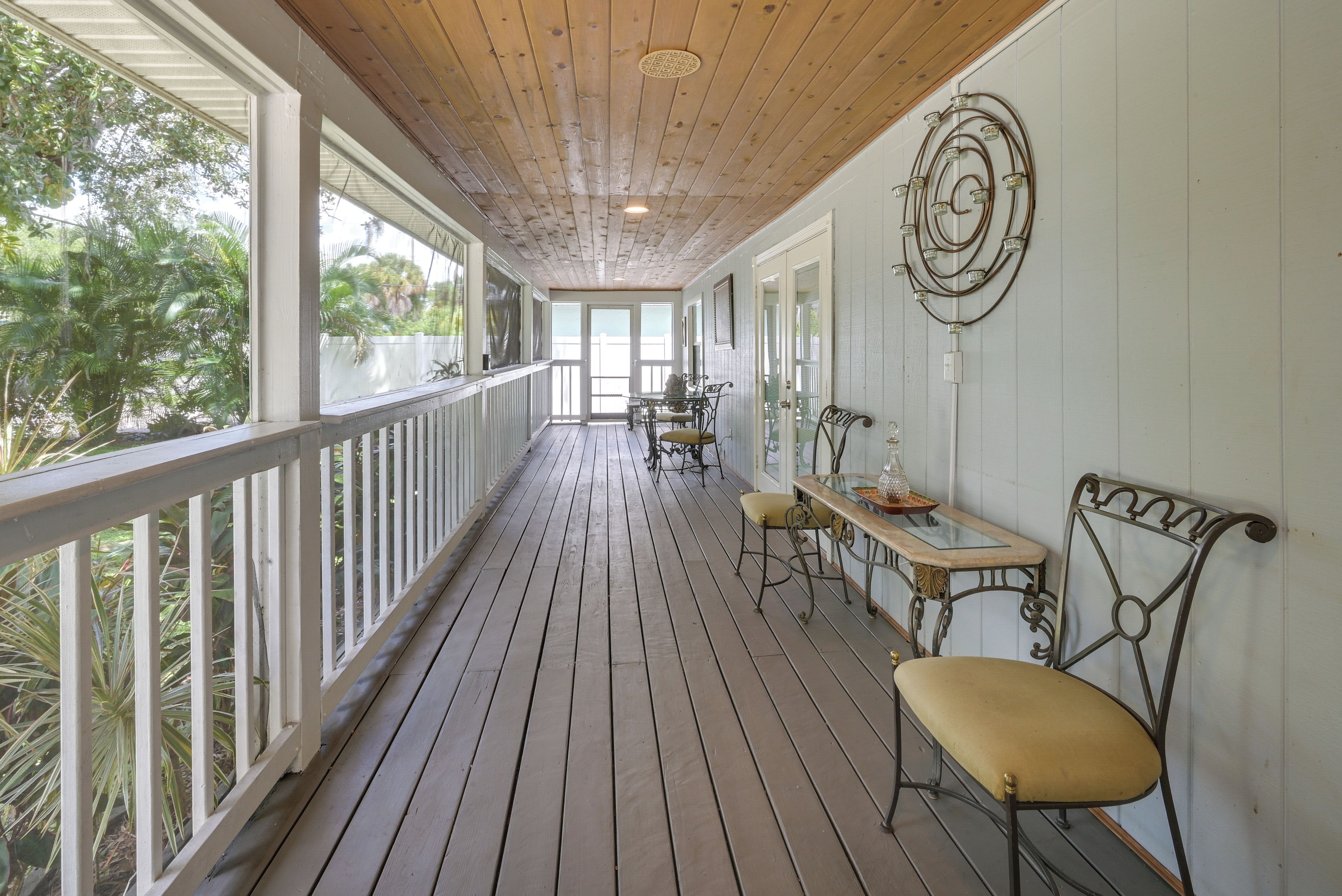 Une terrasse en bois couverte, dotée d’une rambarde, de tables et de chaises, et offrant une vue sur un jardin.
