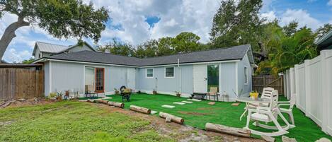 A residential backyard with a lawn, a wooden deck, and a white house with a grey roof.