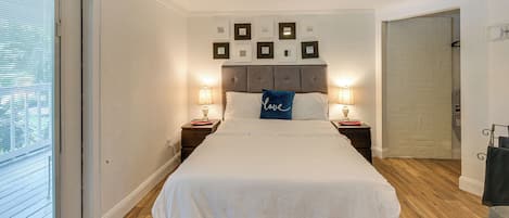 Un dormitorio con una cama grande, dos mesitas de noche con lámparas, una pared con cuadros enmarcados y una puerta corredera hacia un baño.