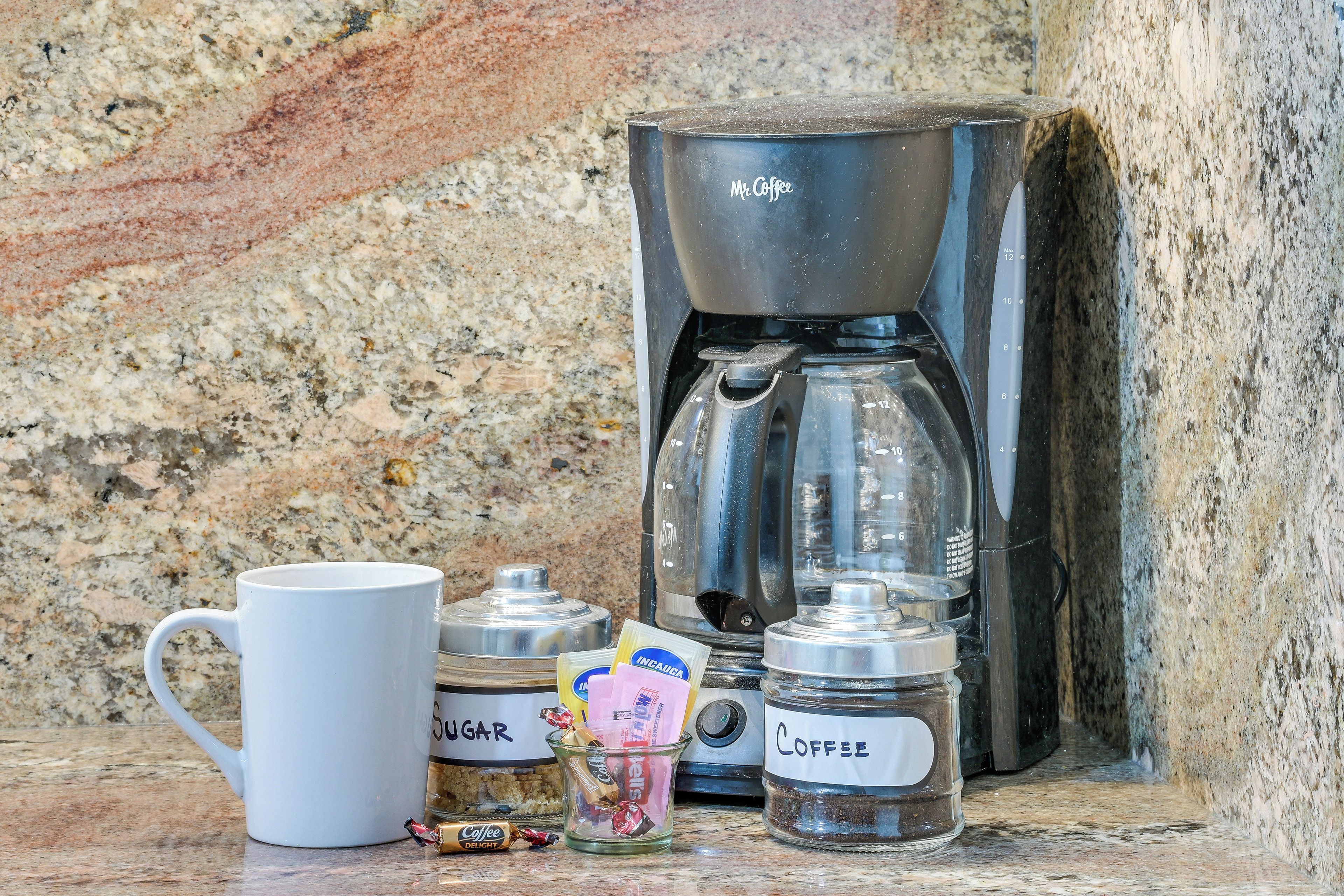 A coffee maker, a mug, sugar, and a jar of coffee on a granite countertop.