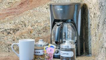 A coffee maker, a mug, sugar, and a jar of coffee on a granite countertop.