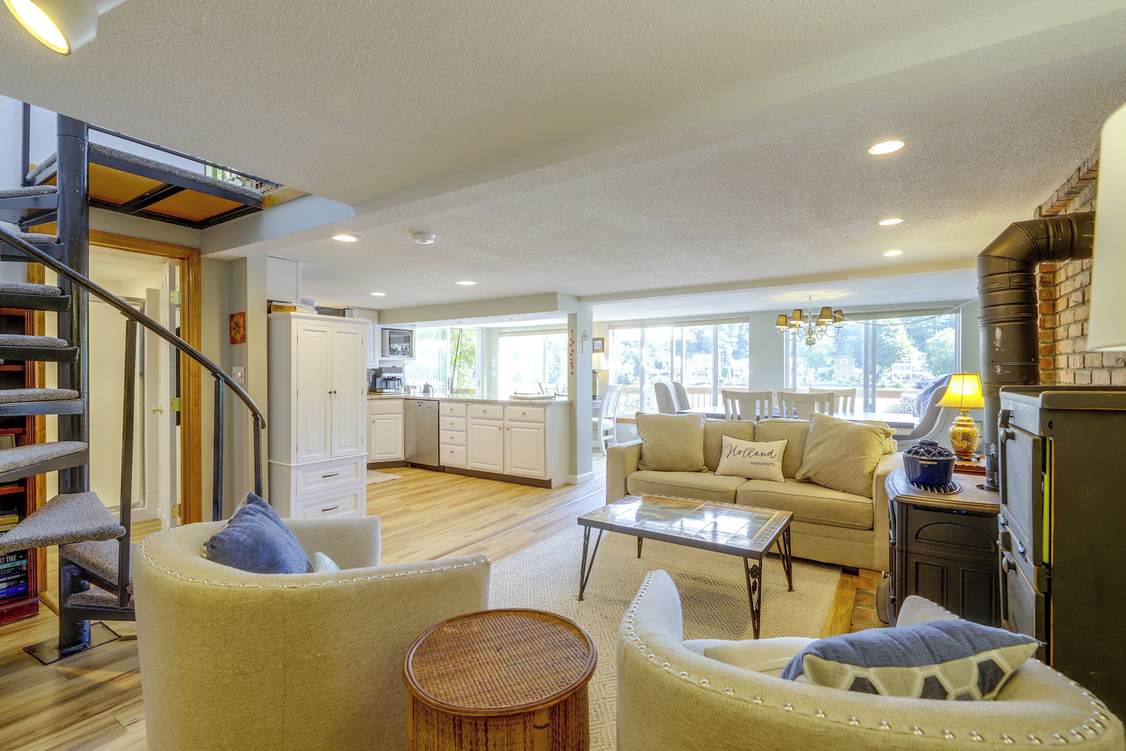 A spacious living area with a staircase, a kitchen in the background, and a sofa with a cushion.