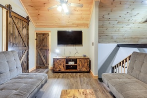 A living room with a wooden ceiling, a mounted TV, and a sliding barn-style door.