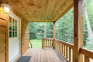 A wooden porch with a railing, a door, and a view of a forested area.