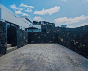 A modern building with a stone wall and a concrete patio. - La Raiz Ocean Views, Volcanic Landscape & Terrace (Tías)
