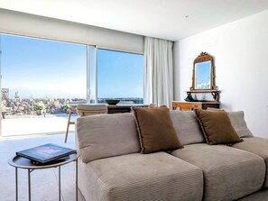 A modern living room with a large window, a sofa, a small table, and a dresser. - La Raiz Ocean Views, Volcanic Landscape & Terrace (Tías)