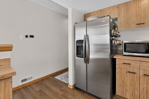 Een keuken met een roestvrijstalen koelkast, een magnetron, houten keukenkastjes en een houten vloer.