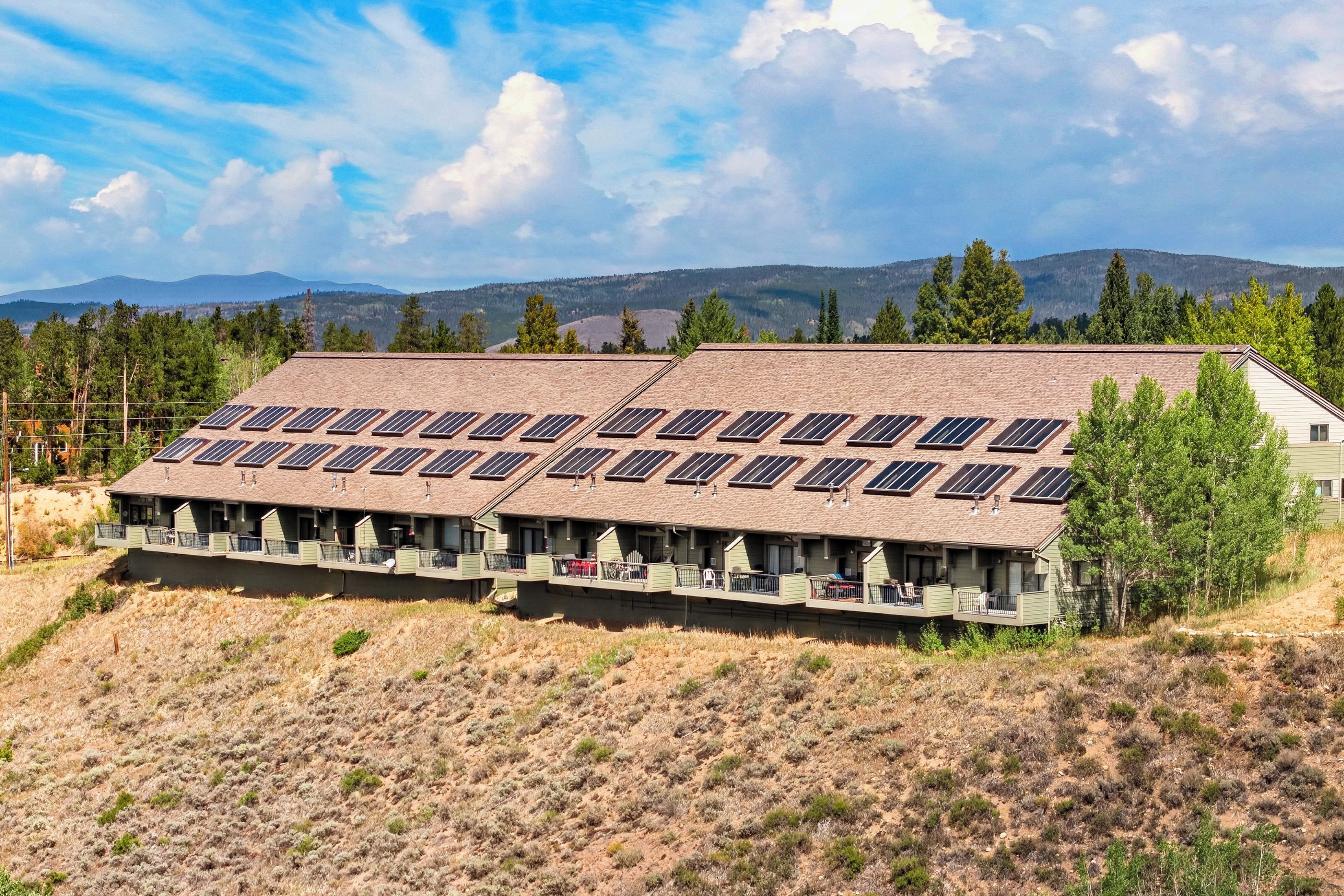 Ein Gebäude mit mehreren Solaranlagen auf dem Dach, umgeben von einer trockenen Landschaft mit vereinzelter Vegetation und fernen Bergen.