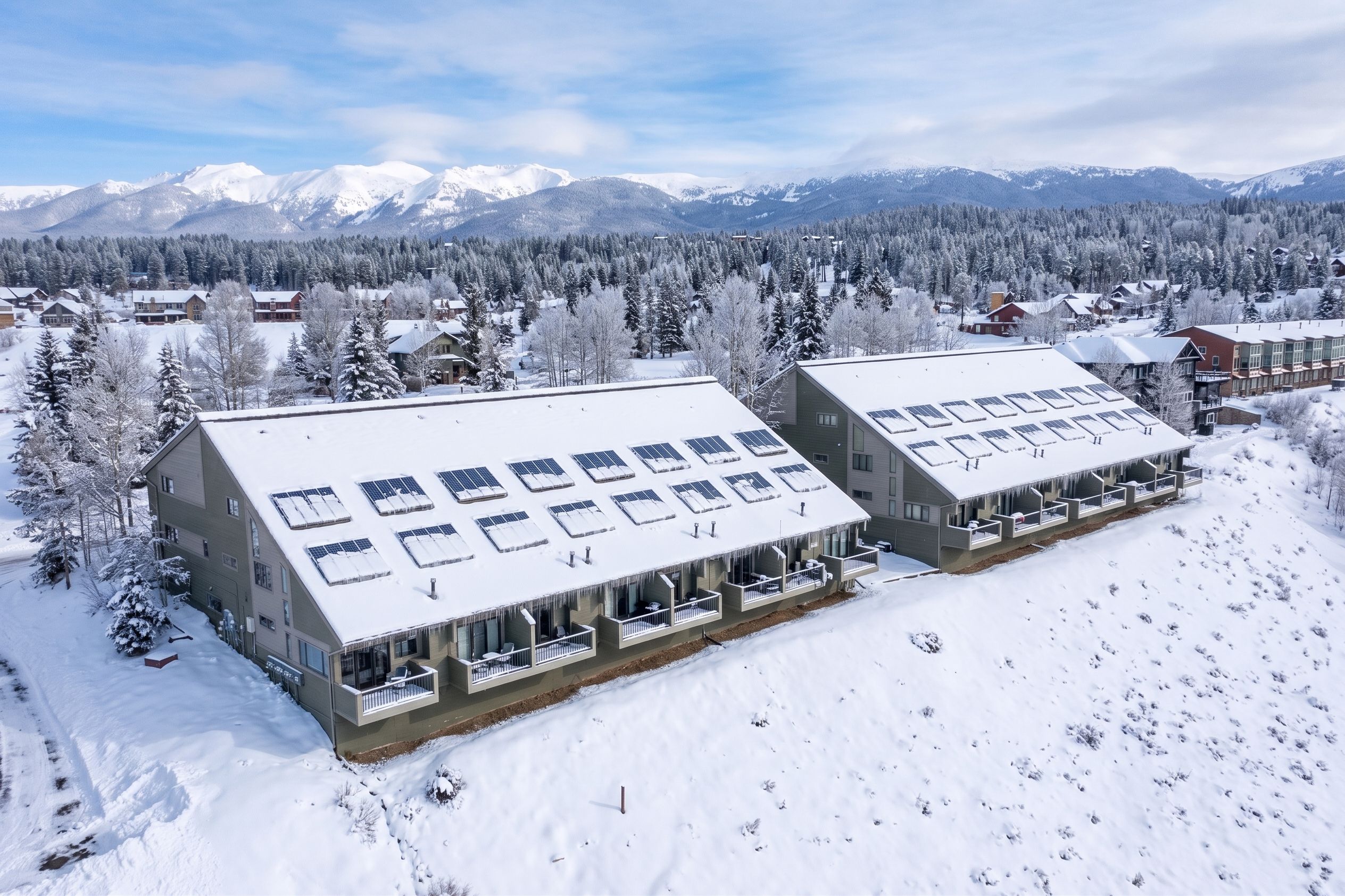 Ein schneebedecktes Gebäude mit zahlreichen Fenstern und Balkonen, umgeben von Wald und Bergen.