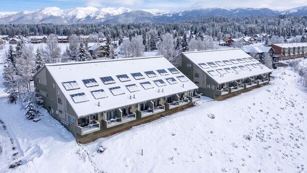 Ein schneebedecktes Gebäude mit zahlreichen Fenstern und Balkonen, umgeben von Wald und Bergen.