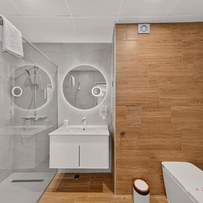 Ein modernes Badezimmer mit Dusche, zwei runden Spiegeln, einem Waschbecken und einer Toilette.