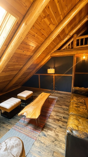 A loft-style room with a sloped ceiling, wooden beams, a sofa, a coffee table, and a patterned rug.