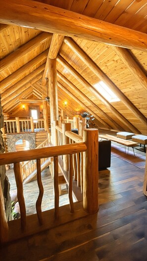 Une chambre mansardée avec des poutres apparentes, un escalier en bois et une vue sur le ciel.