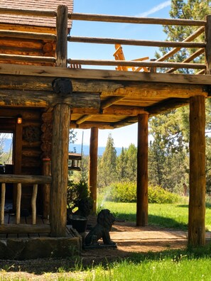 A rustic log cabin with a porch and a view of a forested landscape.
