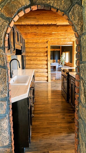 A kitchen with a stone archway, wooden flooring, and modern appliances. - The Chief's Cabin Tumalo 4BR Log Cabin with Cascade Views (Bend)