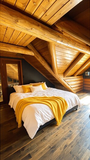 A bedroom with a sloped ceiling, wooden beams, a bed with white bedding and a yellow throw, and a dark wooden floor. - The Chief's Cabin Tumalo 4BR Log Cabin with Cascade Views (Bend)