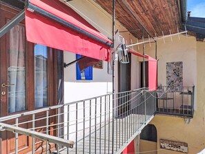 Ein Balkon mit Metallgeländer, einem roten Markisenstoff und Blick auf die Straße darunter.
