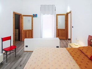 Ein Schlafzimmer mit einem Bett, einem Sessel, einem Nachttisch und einem Fenster mit Vorhängen.