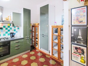 Een keuken met groene kastjes, een betegelde achterwand en een vloer met een rood en geel patroon.