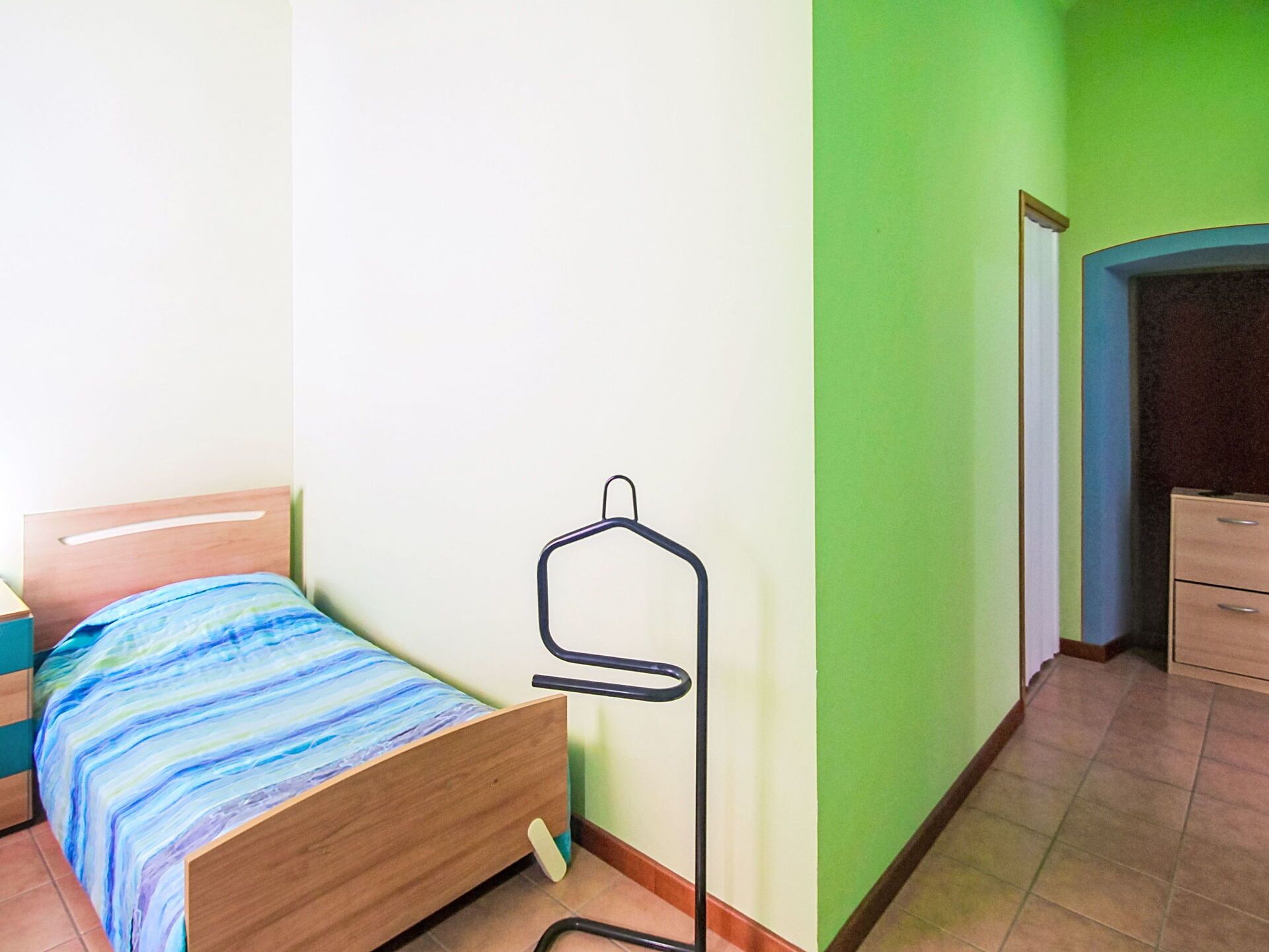 A bedroom with a bed, a hanging clothes rack, a dresser, and a green wall.