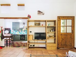 Ein Wohnzimmer mit Fernseher, Holzregalen, einem Essbereich mit Tisch und Stühlen sowie einer Küche im Hintergrund.
