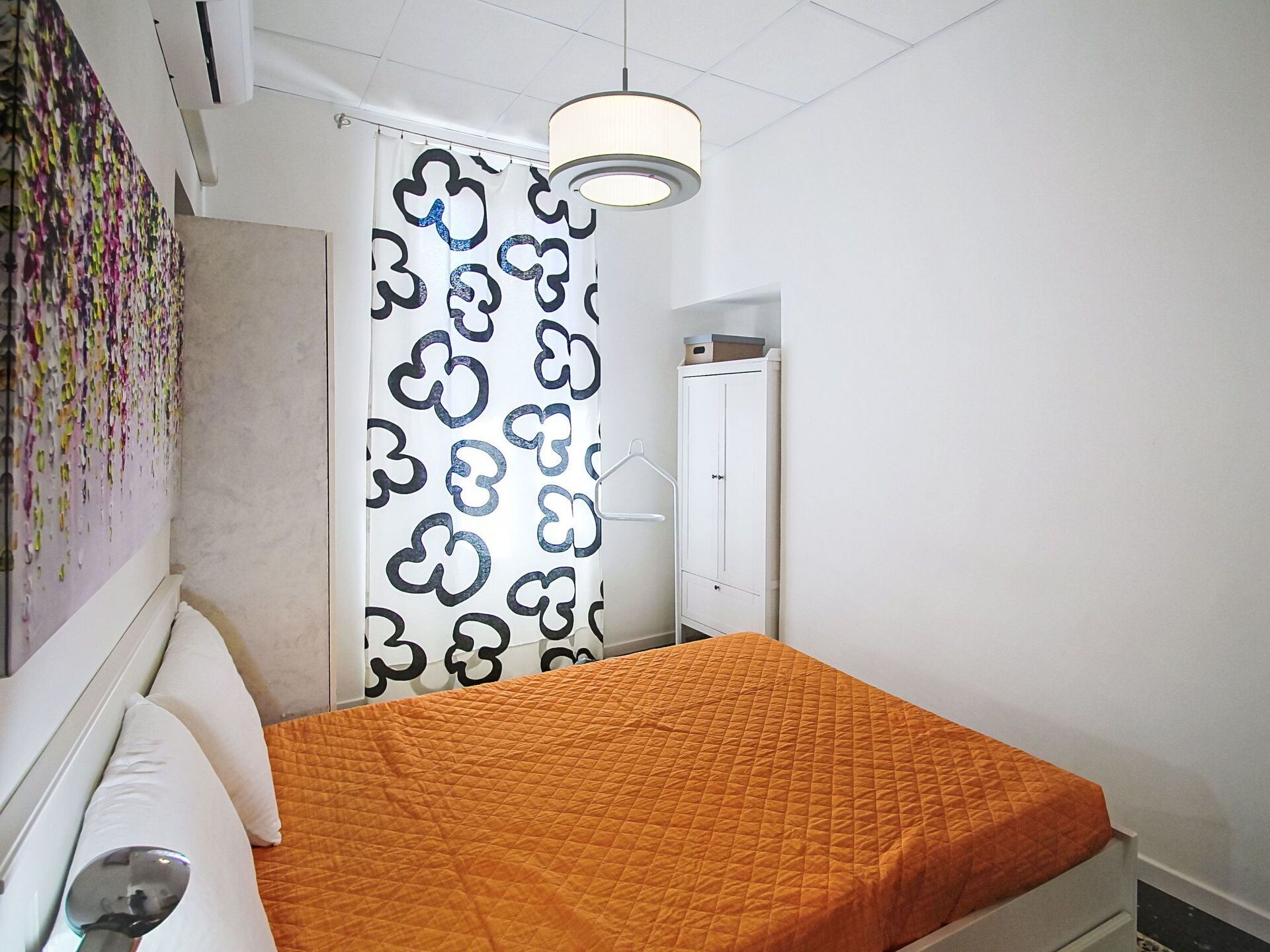 Quarto com cama, luminária pendente, porta e parede com cortina estampada.