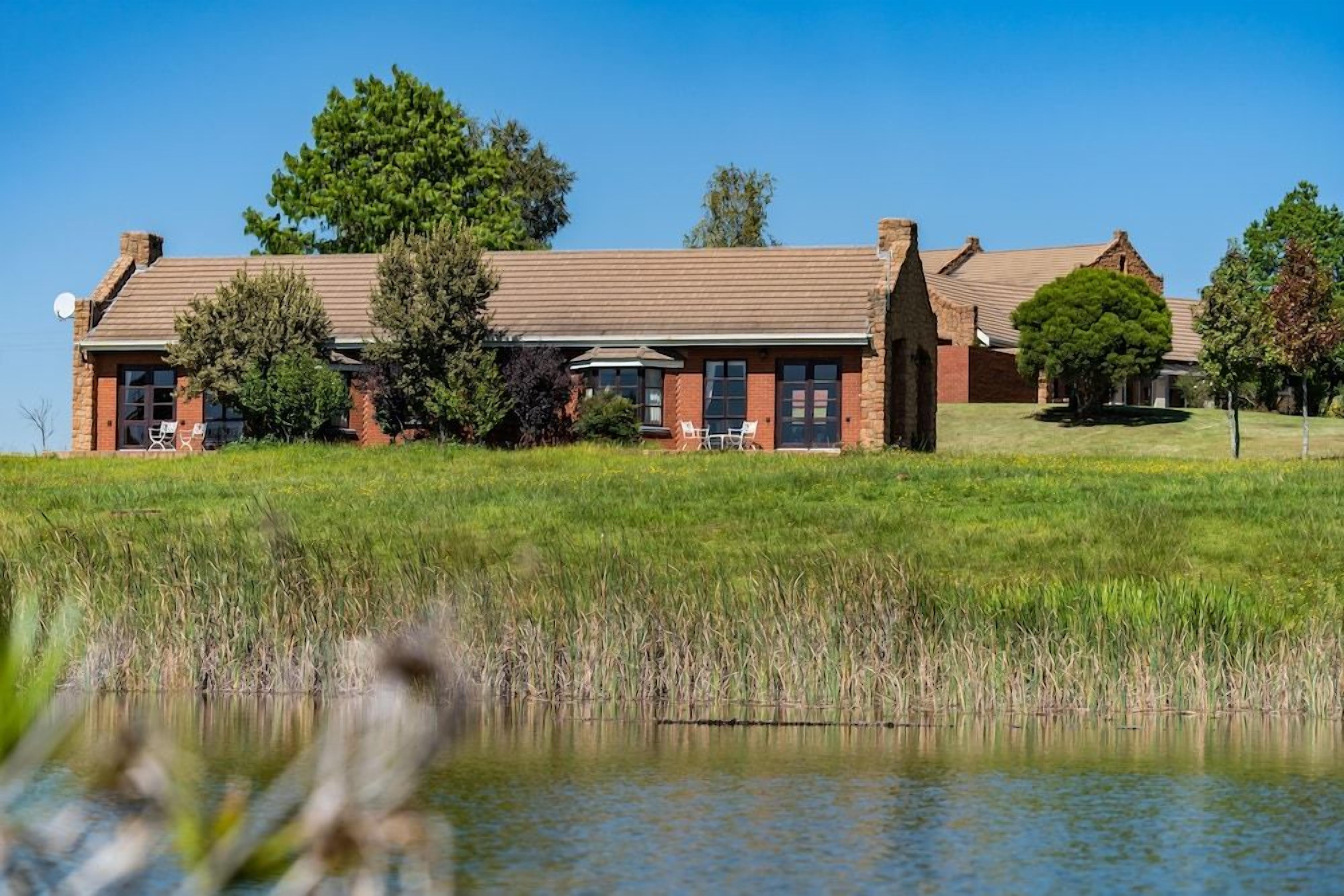 A brick building with a flat roof, surrounded by a grassy field and a body of water.