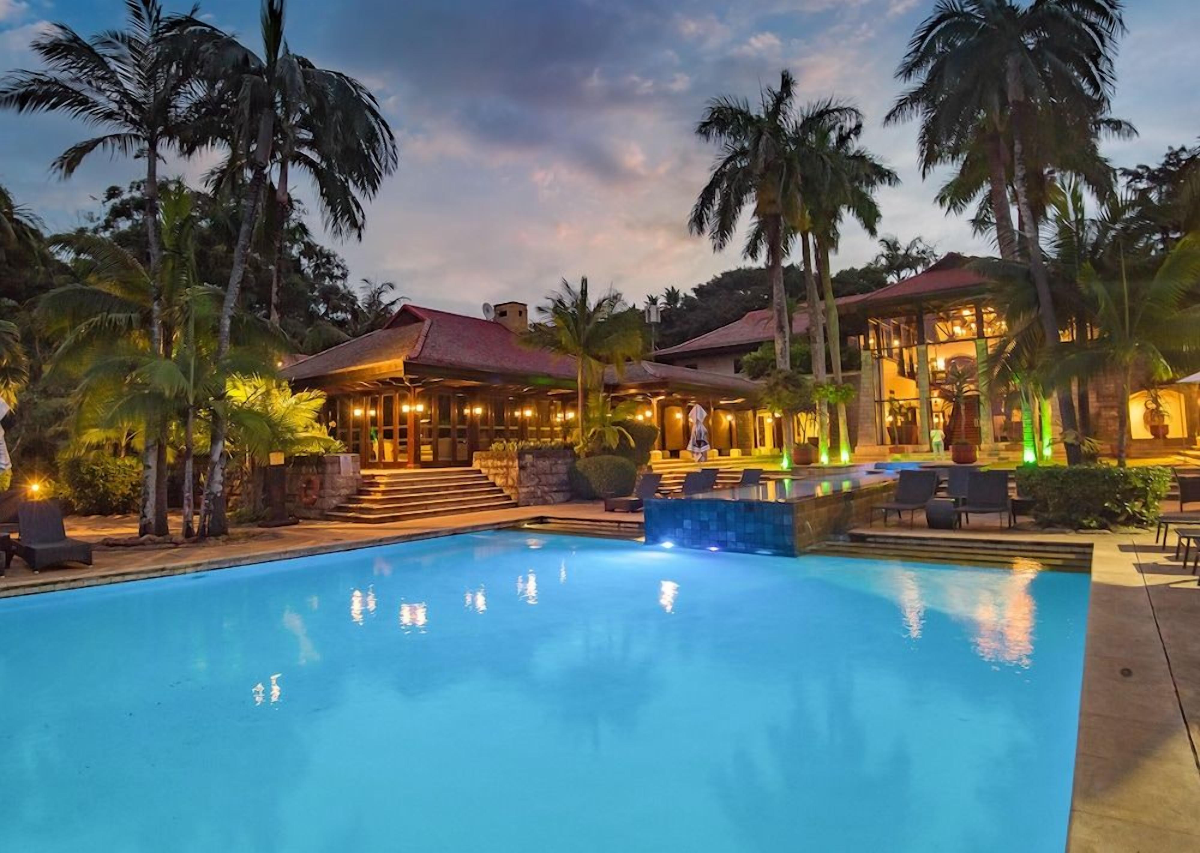 A swimming pool with a building in the background, surrounded by palm trees.