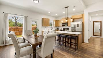 A modern kitchen with wooden cabinets, a central island with bar stools, and a dining area with a large table and chairs.