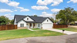 A single-story house with a front garage, a small front porch, and a well-maintained lawn. - Lake House Game Garage - Fire Pit Sleeps 8 (Granbury)
