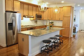 A modern kitchen with wooden cabinets, stainless steel appliances, a granite countertop, and pendant lighting. - Woodlands Haven Bright 3 BR Townhouse in Houston (Spring)