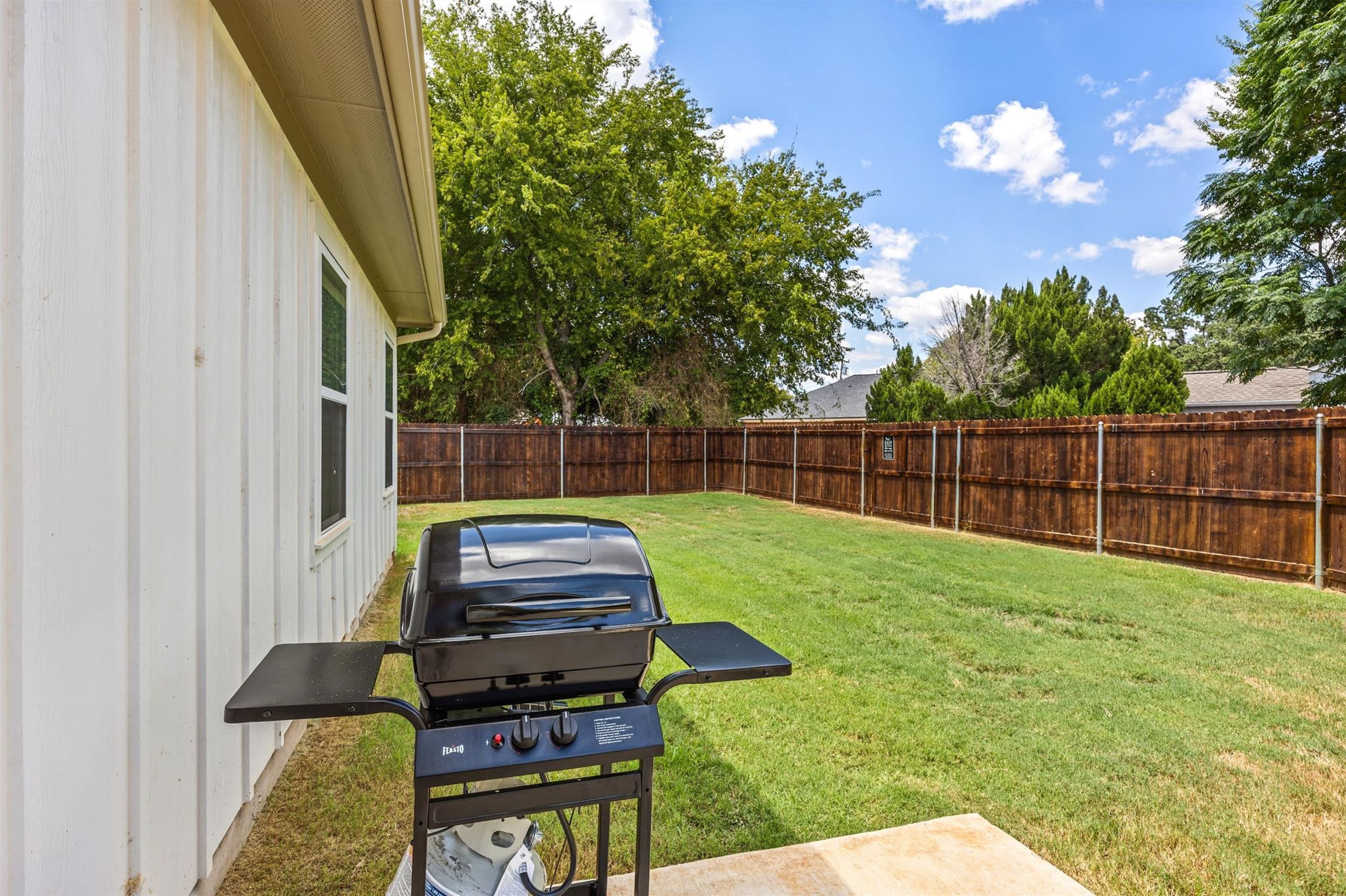 A backyard with a barbecue grill, a wooden fence, and a house.